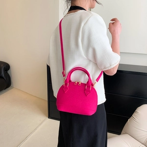 Magenta shell-shaped crossbody bag with lizard pattern and golden hardware shown on model