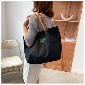 Schulteransicht einer schwarzen Canvas-Einkaufstasche mit braunen Ledergriffen und Logo
