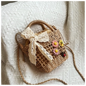 Detail of woven straw handbag featuring lace bow, plush flowers and drawstring lining