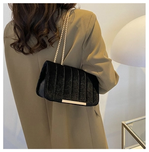 Close-up of black velvet crossbody bag with gold chain strap on a khaki blazer