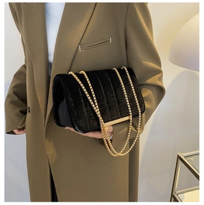 Detail of black velvet crossbody bag featuring vertical quilting and gold chain strap