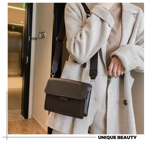 Detail einer minimalistischen dunkelbraunen Tasche mit breitem Gurt auf beigem Mantel