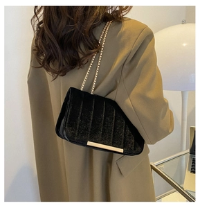 Détail du sac à rabat en velours noir avec chaîne dorée et bordure métallique à la base