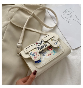 Détail du sac bandoulière crème avec motifs graffiti et texture cuir de litchi