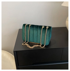 Détail d'un sac bandoulière en velours vert foncé avec coutures verticales et chaîne dorée