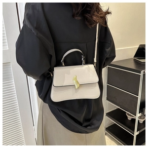 Detail of a beige trapezoid crossbody bag with a golden wave twist lock and contrast edging