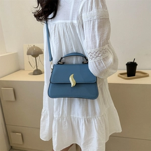 Chic blue leather handbag with gold wavy clasp shown in a lifestyle model setting