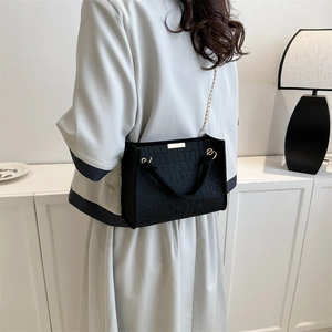Black crocodile pattern crossbody bag with gold chain strap shown on model in minimal interior