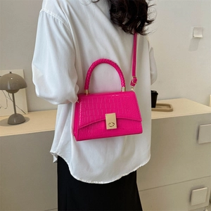 Pink crocodile-embossed handbag with woven handle and gold clasp on a model