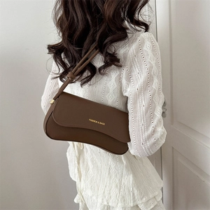 Minimalist brown leather baguette shoulder bag shown as worn by model in soft lighting