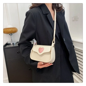 Schicke beige Umhängetasche mit rosa Herz-Detail, präsentiert auf einem schwarzen Blazer