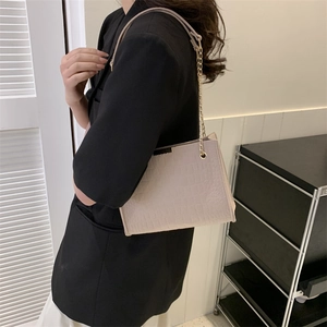 Pink crocodile pattern shoulder bag with a gold chain strap worn by a female model