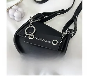 Détail du sac selle en simili cuir noir avec chaînes argentées sur un fond de tissu blanc pur