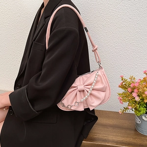 Sac bandoulière rose avec nœud et chaîne en perles porté par un mannequin en costume