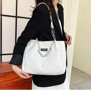 Détail d'un sac cabas blanc avec texture florale 3D, chaîne en perles et étiquette