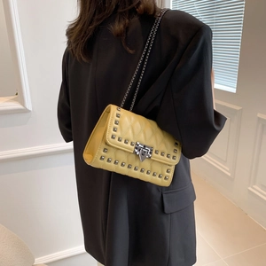 Yellow quilted chain bag with grey studs on a woman wearing a black blazer