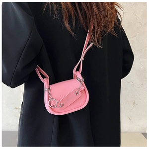 Détail d'un mini sac selle rose avec chaîne en métal argenté sur un blazer noir