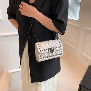 White quilted crossbody bag with dark rivets and chain strap worn by a model in a black suit