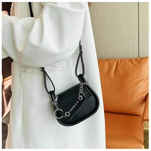 Détail du sac à selle noir avec chaîne dorée et étiquette de mode sur un manteau blanc