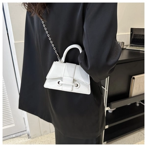 Close-up of white patent leather mini bag with metal chain strap on black suit