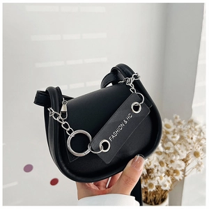 Détail d'un sac besace en cuir noir mat avec chaîne argentée et étiquette déco