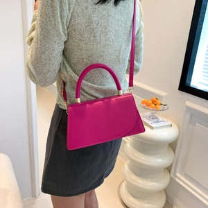 Fuchsia pink structured crossbody bag with top handle shown on a model in a modern interior