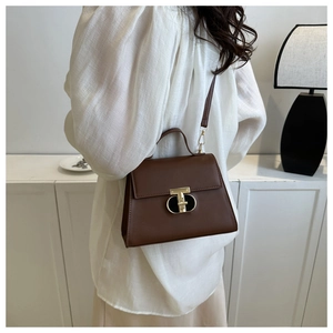 Dettaglio borsa in pelle marrone con chiusura a T dorata su sfondo mobile bianco