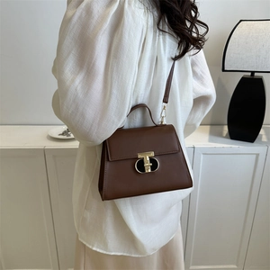 Dunkelbraune Lederhandtasche mit goldenem T-Verschluss an einem Model präsentiert