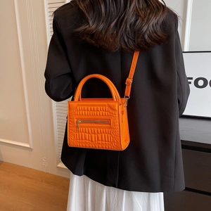 Orange faux crocodile leather handbag with metal zip detail shown on shoulder of a model