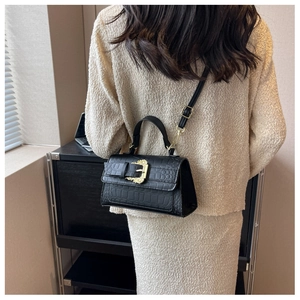 Close-up of black croc-effect handbag with ornate golden vintage buckle on beige fabric