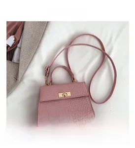 Detail of pink croc-embossed crossbody bag with golden twist lock on white fabric