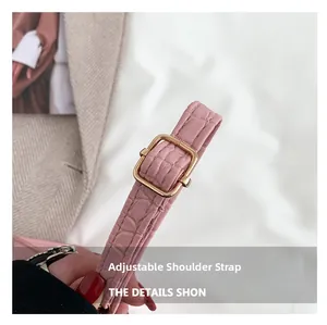 Detail of adjustable pink crocodile embossed leather shoulder strap with golden metal buckle