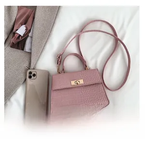 Detail of pink croc-embossed small square bag featuring a gold twist lock and top handle
