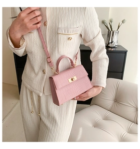 Detail shot of a pink crocodile-embossed handbag featuring a gold turn-lock and sturdy handle