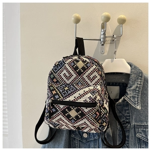 Detailed close-up of a small ethnic backpack with colorful woven geometric patterns on white wall