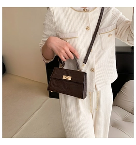 Detail of dark brown croc-pattern mini square bag with elegant gold twist lock and handle