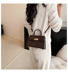 Detail of dark brown crocodile pattern crossbody bag with golden twist lock on a model