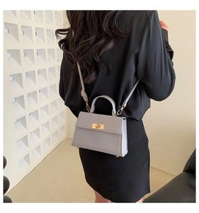 Gray crocodile pattern crossbody bag with gold rotating lock shown on person