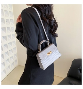 Detail of light gray croc-embossed crossbody bag with gold buckle on model's shoulder