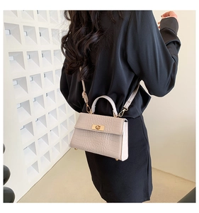 Detail of beige crocodile embossed leather bag with golden twist lock on model back