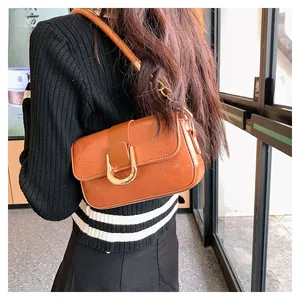 Detail of a brown crocodile pattern shoulder bag with a gold horseshoe buckle on a model