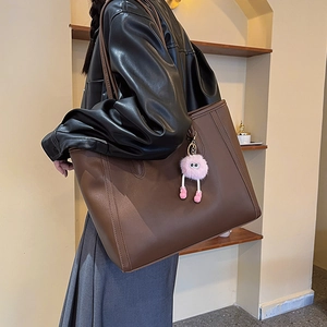 Große braune Leder-Einkaufstasche mit rosa Plüschanhänger an der Schulter des Models