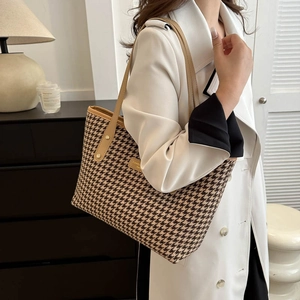 Classic houndstooth tote bag with brown leather handles worn by a model in a white coat