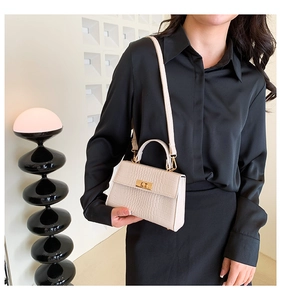 Detail of cream faux crocodile texture shoulder bag with gold metal clasp on black shirt