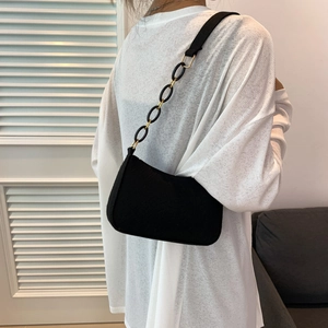 Minimalist black underarm bag with decorative gold chain strap shown on model shoulder