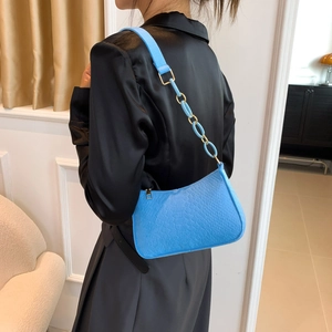 Blue snake skin baguette bag with gold chain strap worn on shoulder in a cozy interior