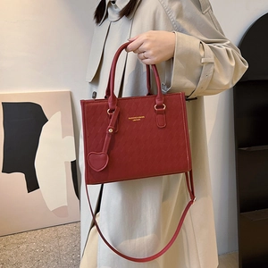 Red quilted tote bag with heart pendant and adjustable strap in a modern home setting