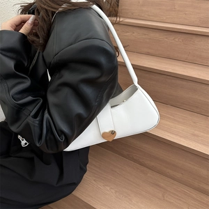 White minimalist leather underarm bag with gold heart buckle shown on model at a side view