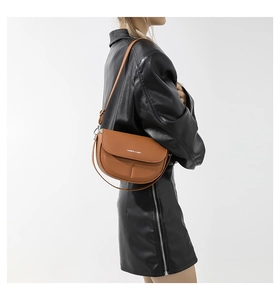 Vista dettagliata della borsa a sella in pelle marrone con scritte bianche su outfit nero