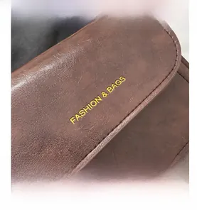 Gros plan détaillé du sac besace en cuir PU marron foncé avec logo doré et surpiqûres